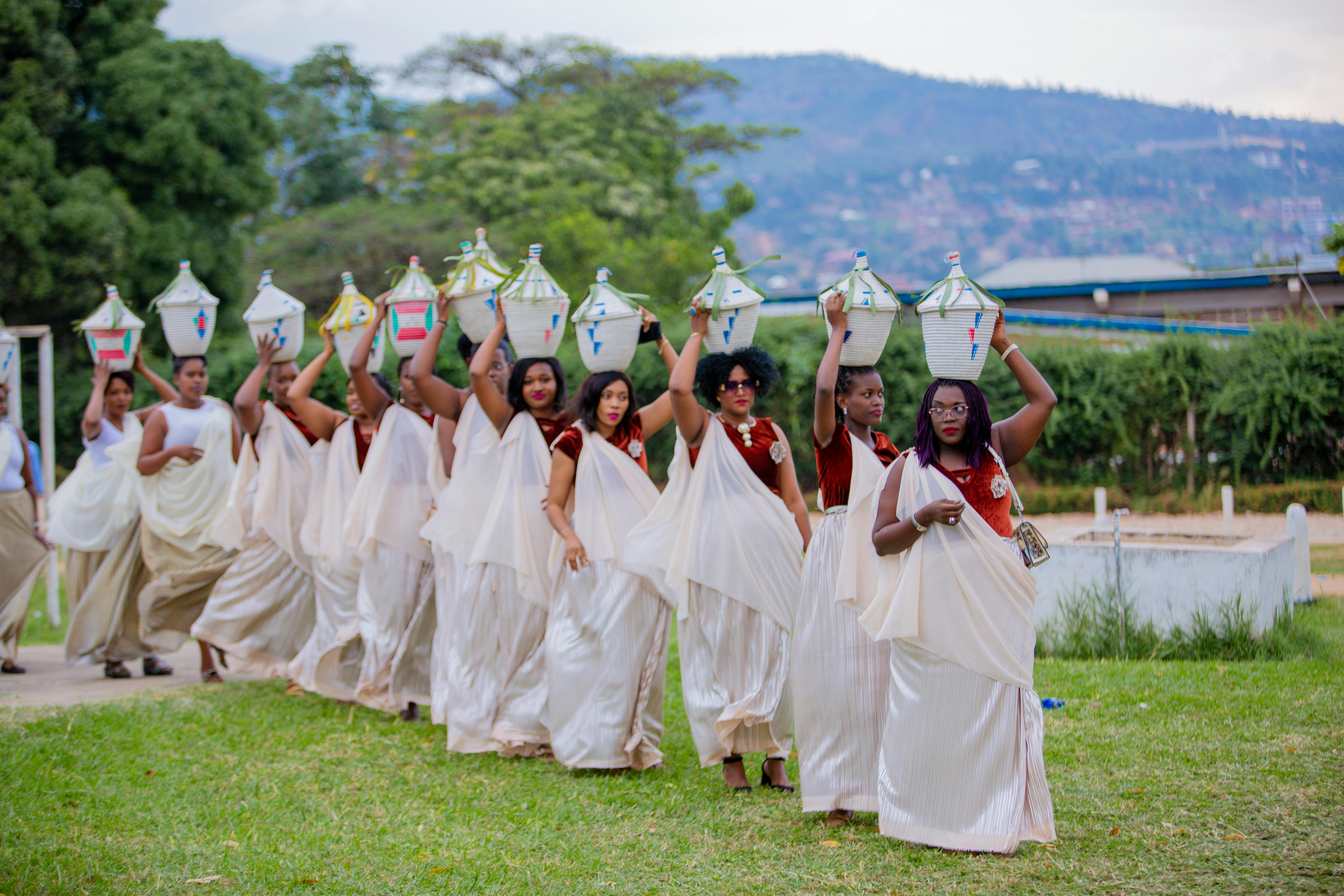Group of African women in traditional dress carrying colorful baskets in an outdoor cultural ceremony.