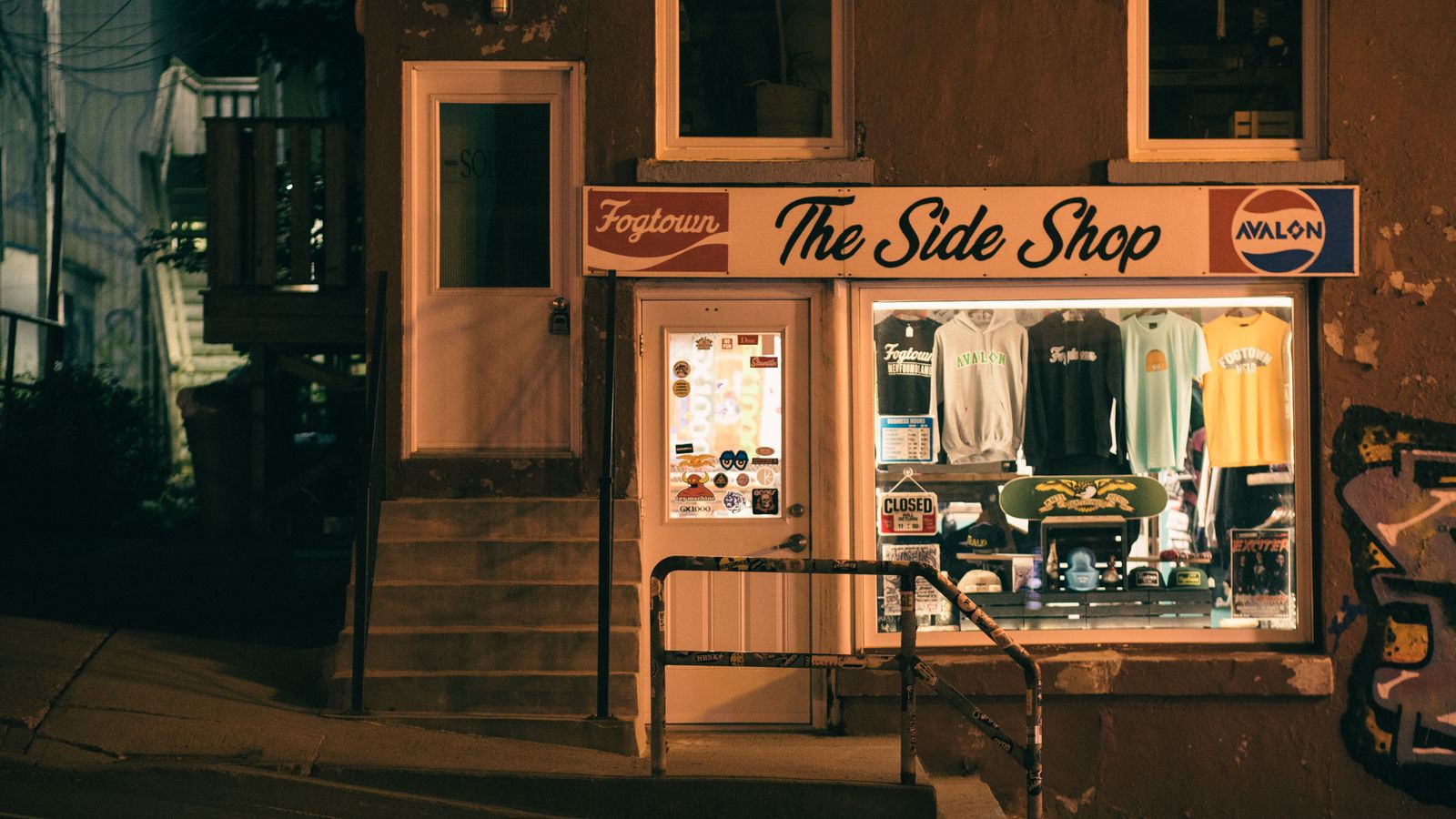 Warm, illuminated storefront of The Side Shop at night, showcasing apparel and signage.