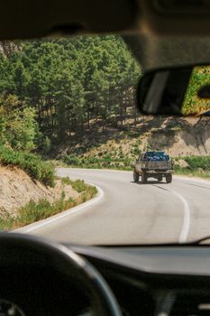 A rugged truck navigates a winding mountain road through lush pine trees on a sunny day.