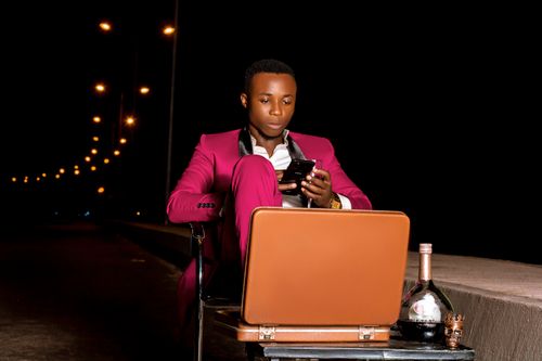 Free Sophisticated man in a pink suit sitting with a briefcase and whiskey at night. High style and elegance. Stock Photo