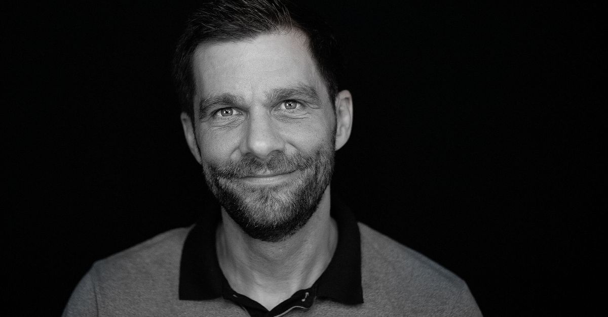 Close-up black and white portrait of a smiling bearded man against a dark background