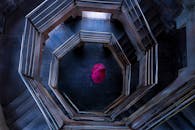 从上方拍摄的艺术镜头中，一把粉红色的伞出现在螺旋楼梯上