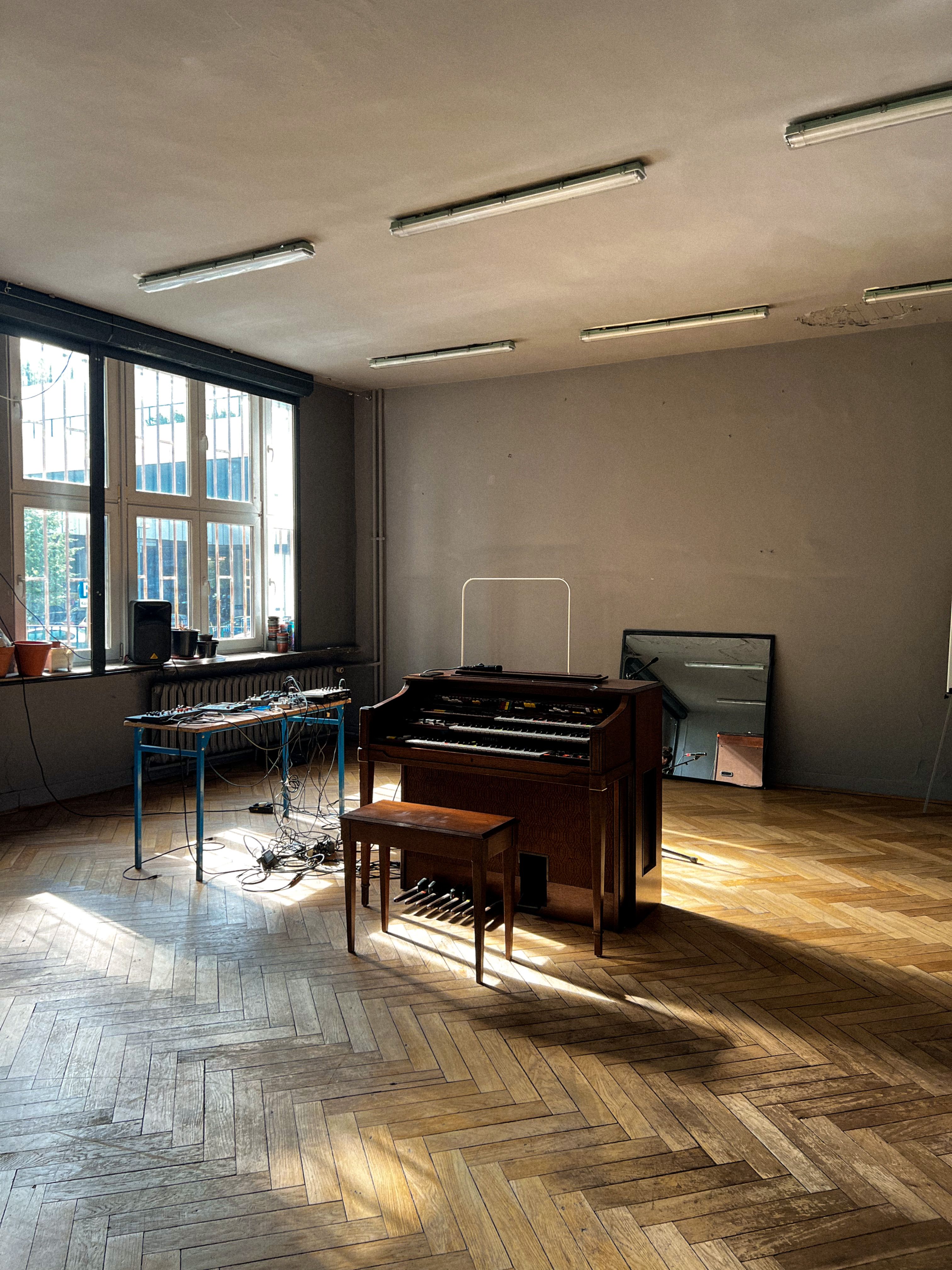 Spacious music room featuring a piano, mirror, and sunlight casting shadows across wooden floors.