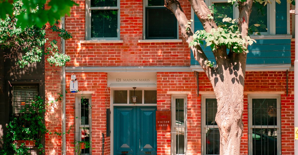 A picturesque brick townhouse with a vibrant blue door and lush tree.