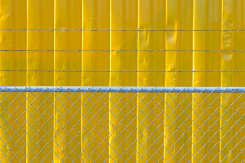 Free Close-up of a yellow metal wall with barbed wires and a chain link fence for security. Stock Photo