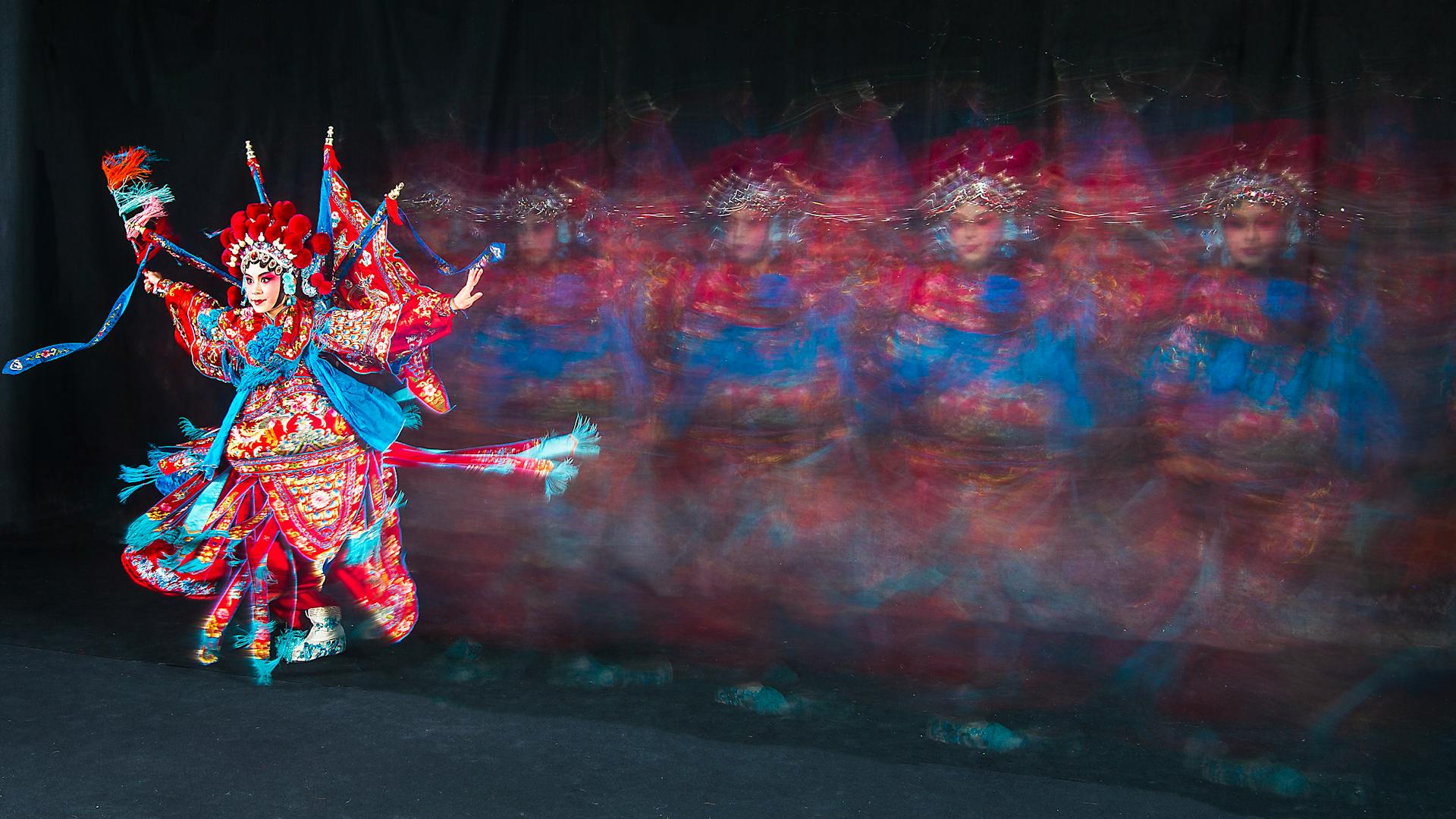 Asian opera performer in colorful traditional attire, captured in motion on stage.