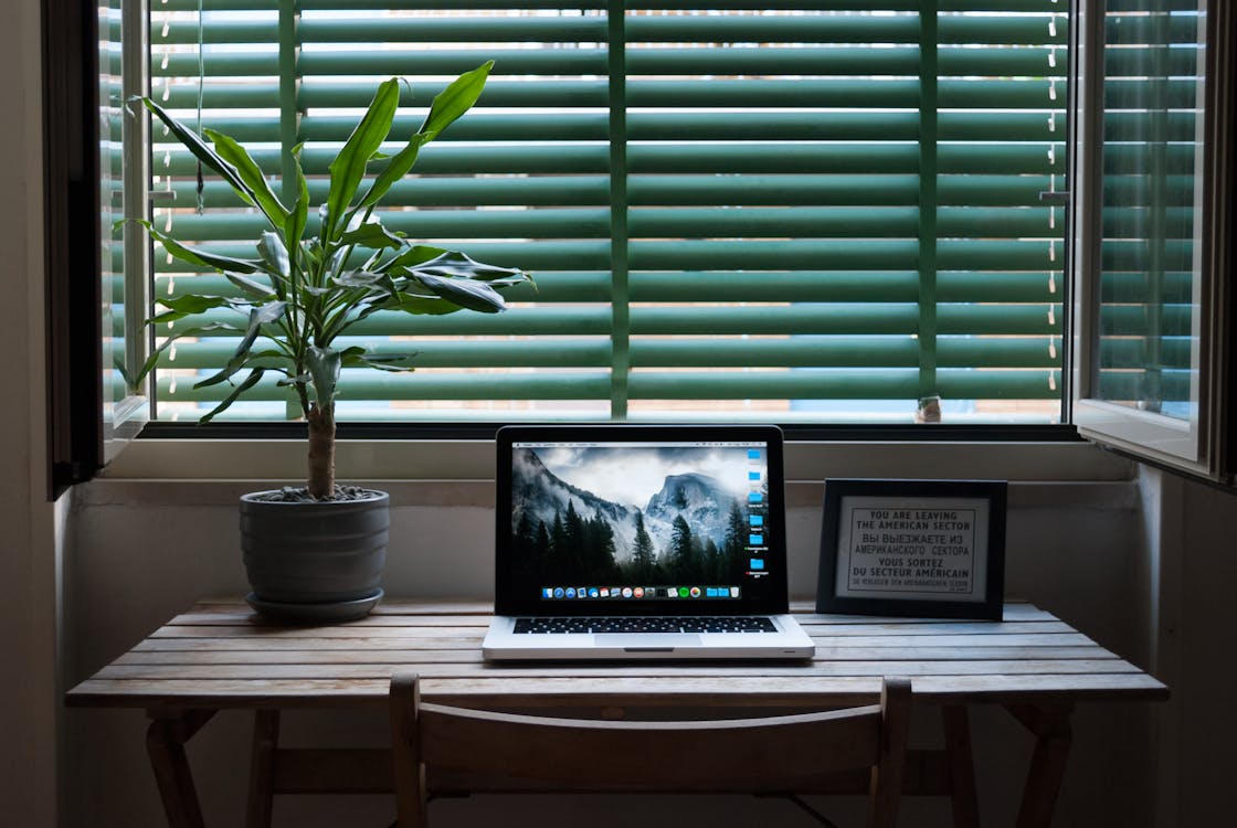 Free Photo of Macbook Air on a Table Next to House Plant and Picture Frame. Stock Photo