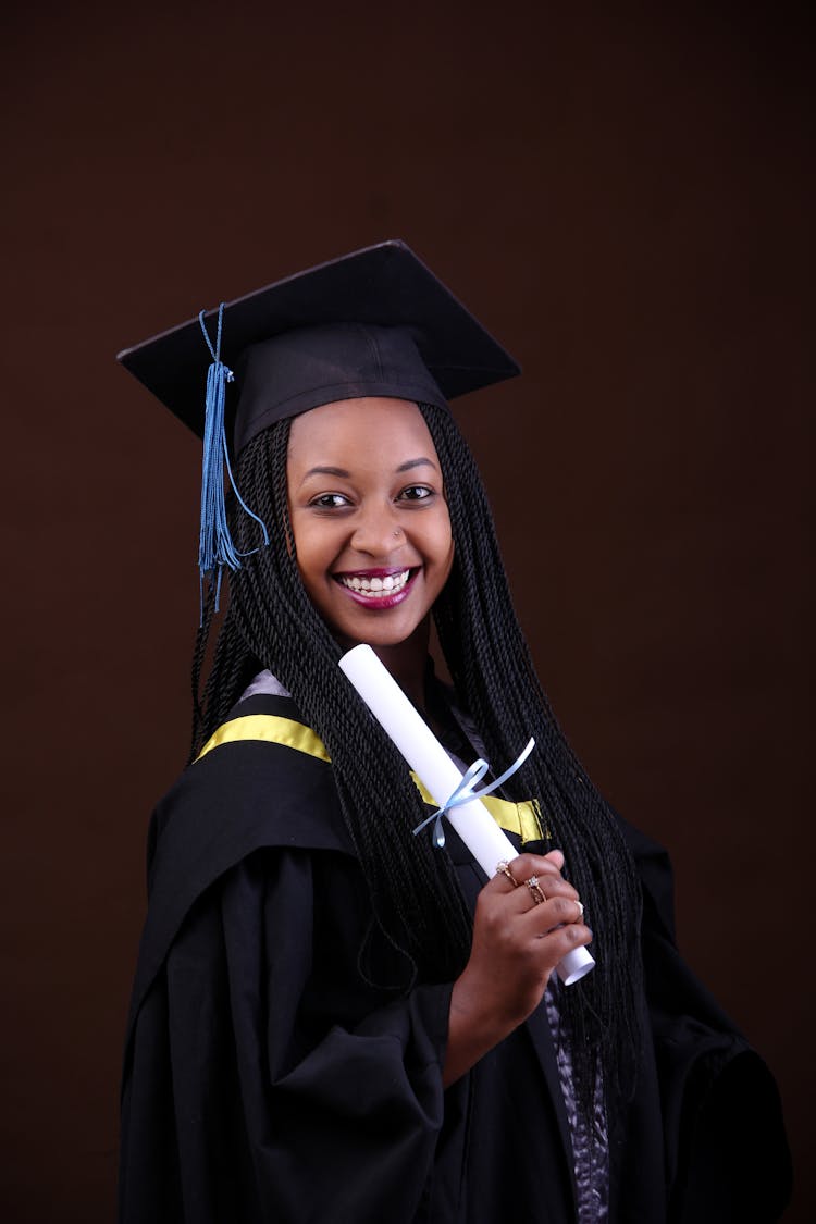 A Woman In Academic Dress And Mortarboard Hat Holding A Diploma