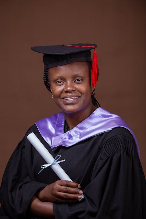 Free Smiling Woman in Academic Dress Holding a Diploma Stock Photo