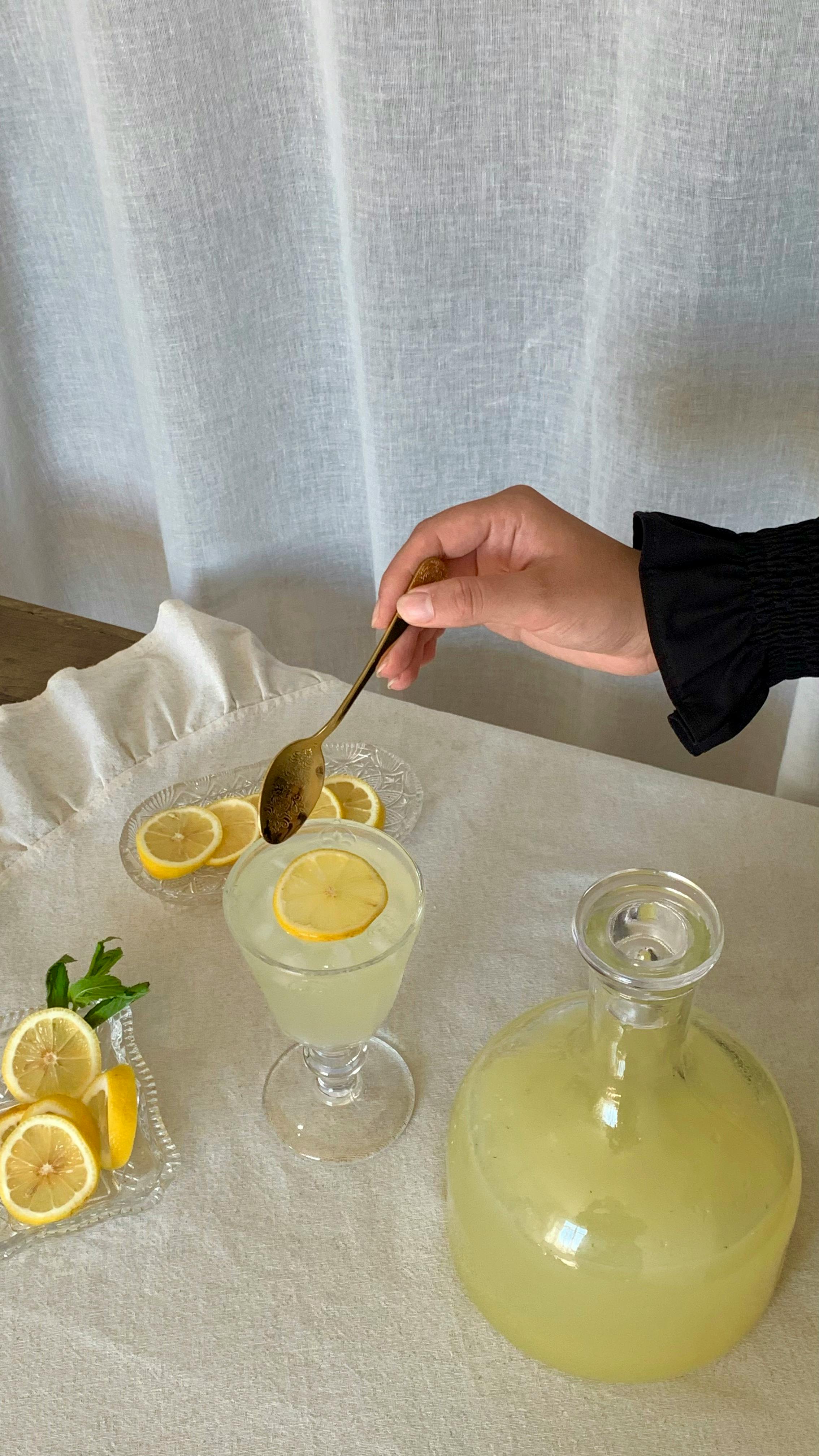 hand with a spoon above a glass of lemonade