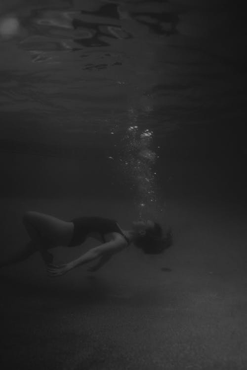 Black and White Photo of a Woman in a Swimsuit Swimming Underwater