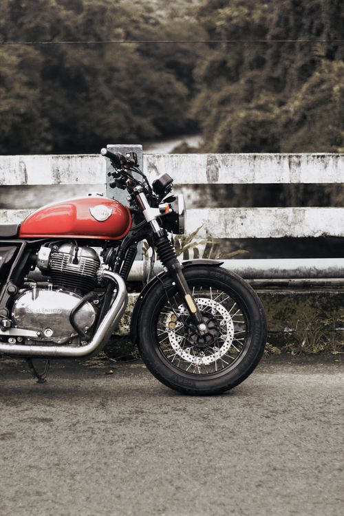 Free A vintage red motorcycle parked against a weathered, rustic bridge with greenery in the background. Stock Photo