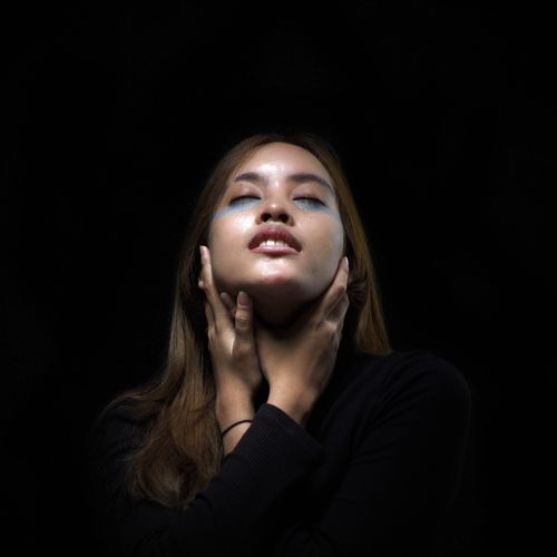 Free Close-up portrait of a woman with artistic makeup and eyes closed against a black background. Stock Photo