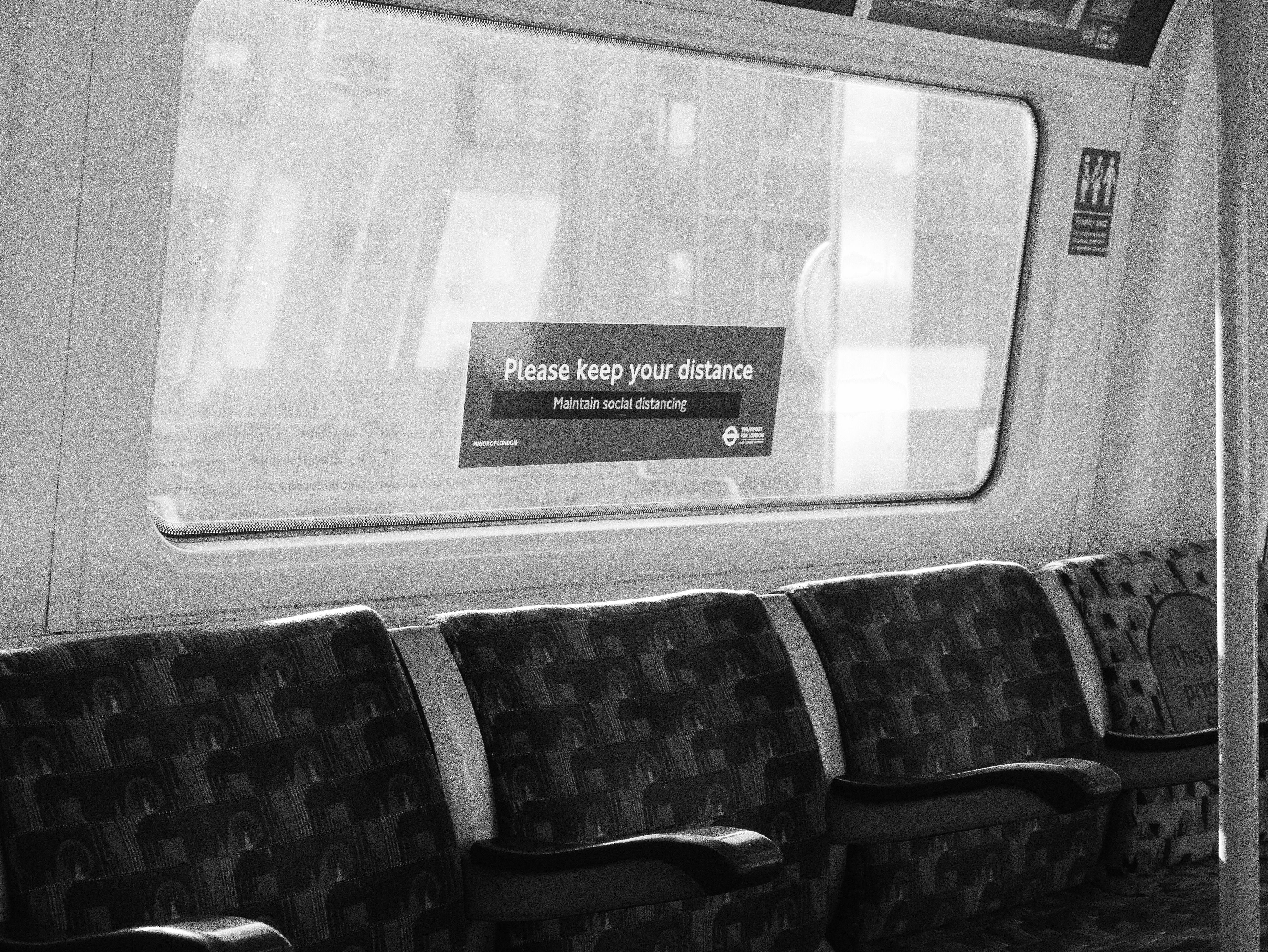 Black and white photo of empty subway seats with a social distancing sign on the window.