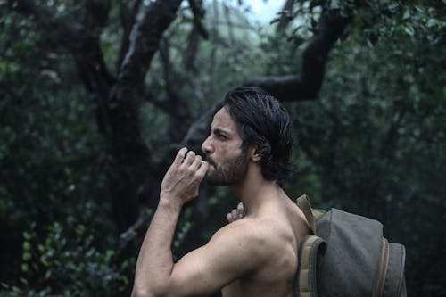 Side View of a Topless Man Smoking Cigarette while Carrying His Backpack