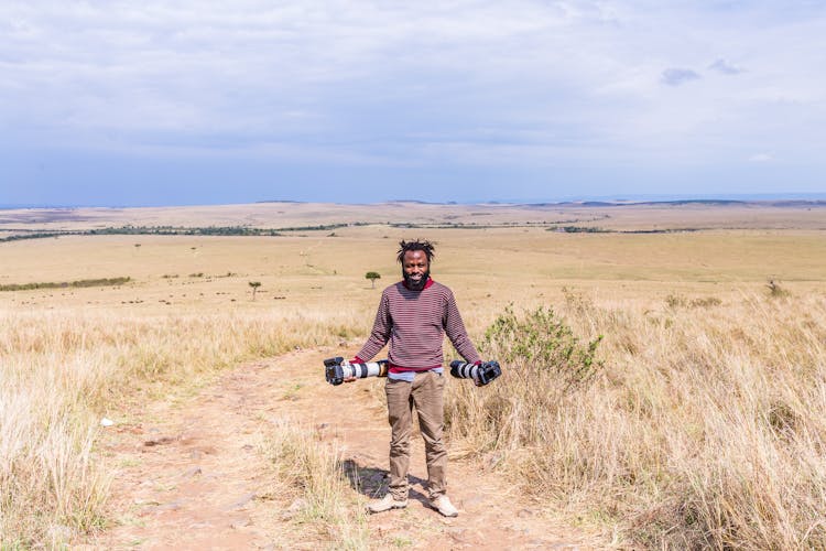 Man Holding Professional Cameras On A Field 