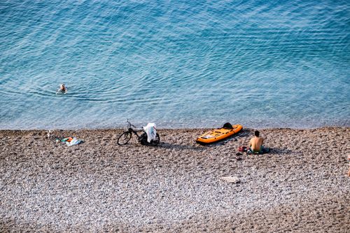 Free Aerial view of a man enjoying a sunny day on a pebble beach with clear sea waters, bike, and paddleboard. Stock Photo