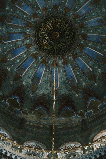 A detailed view of a mosque's ornate ceiling showcasing beautiful Arabic calligraphy and intricate patterns.