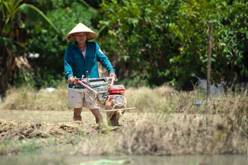 A Man in Blue Long Sleeves Using Hand Held Plowing Machine