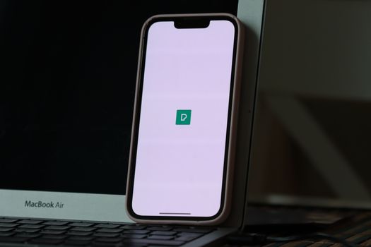 Smartphone resting against a laptop screen with app icon displayed, indoors.