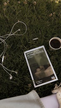 A book, headphones, and coffee on a grassy park setting, ideal for leisure and relaxation.