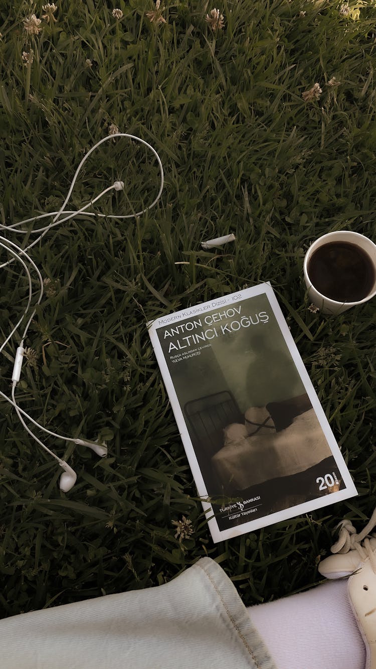 Person Relaxing On Grass With Tea, Catalogue, And Music 