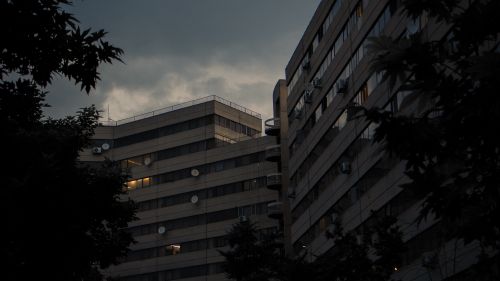 Free Dark and moody image of urban buildings with lit windows during dusk, emphasizing architectural design. Stock Photo