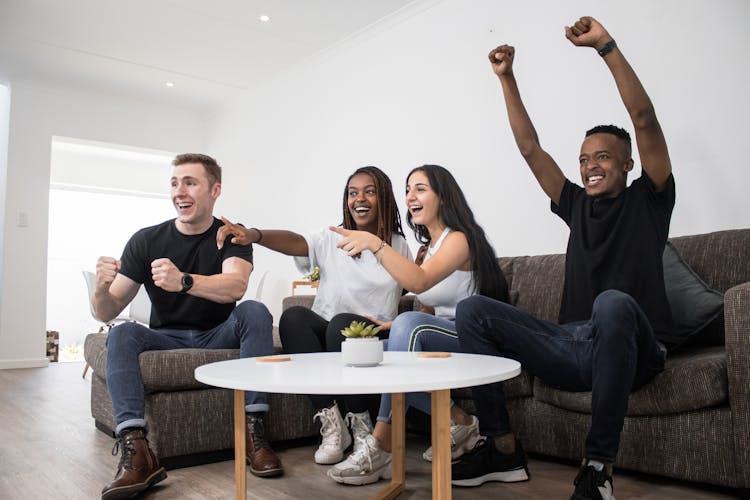 Friends Cheering While Watching TV On Couch