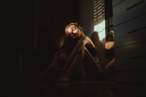 Free A woman sits indoors bathed in dramatic light and shadows, creating an introspective mood. Stock Photo