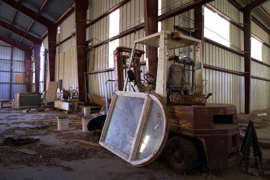 An old, rusty forklift sits in a deserted warehouse filled with debris and obsolete equipment.