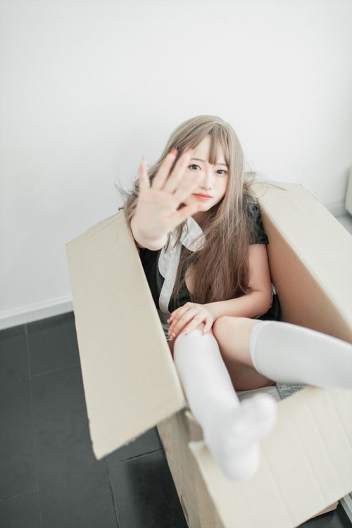 Free A young woman with long hair sitting playfully inside a cardboard box indoors. Stock Photo