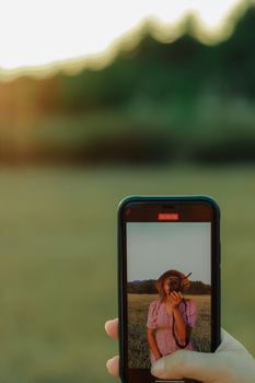 Close-up of a person using a smartphone to capture a sunset photograph, emphasizing depth of field.