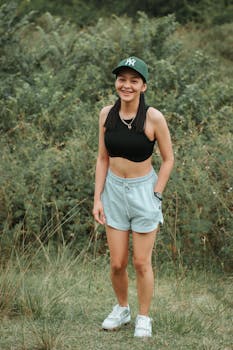 Smiling young woman in casual summer outfit posing outdoors in a grassy field.