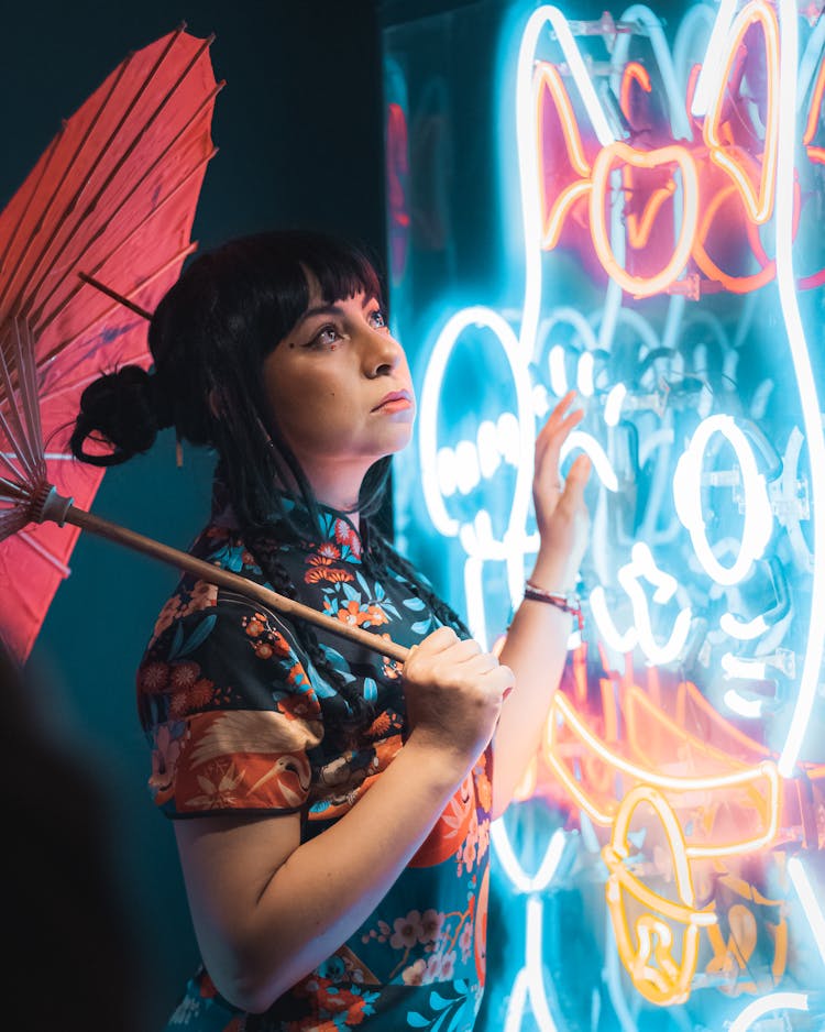 Woman With Paper Umbrella Touching Bright Neon Sign