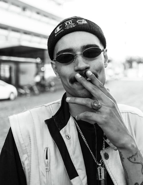 Grayscale Photo of a Man Wearing Sunglasses while Smoking Cigarette