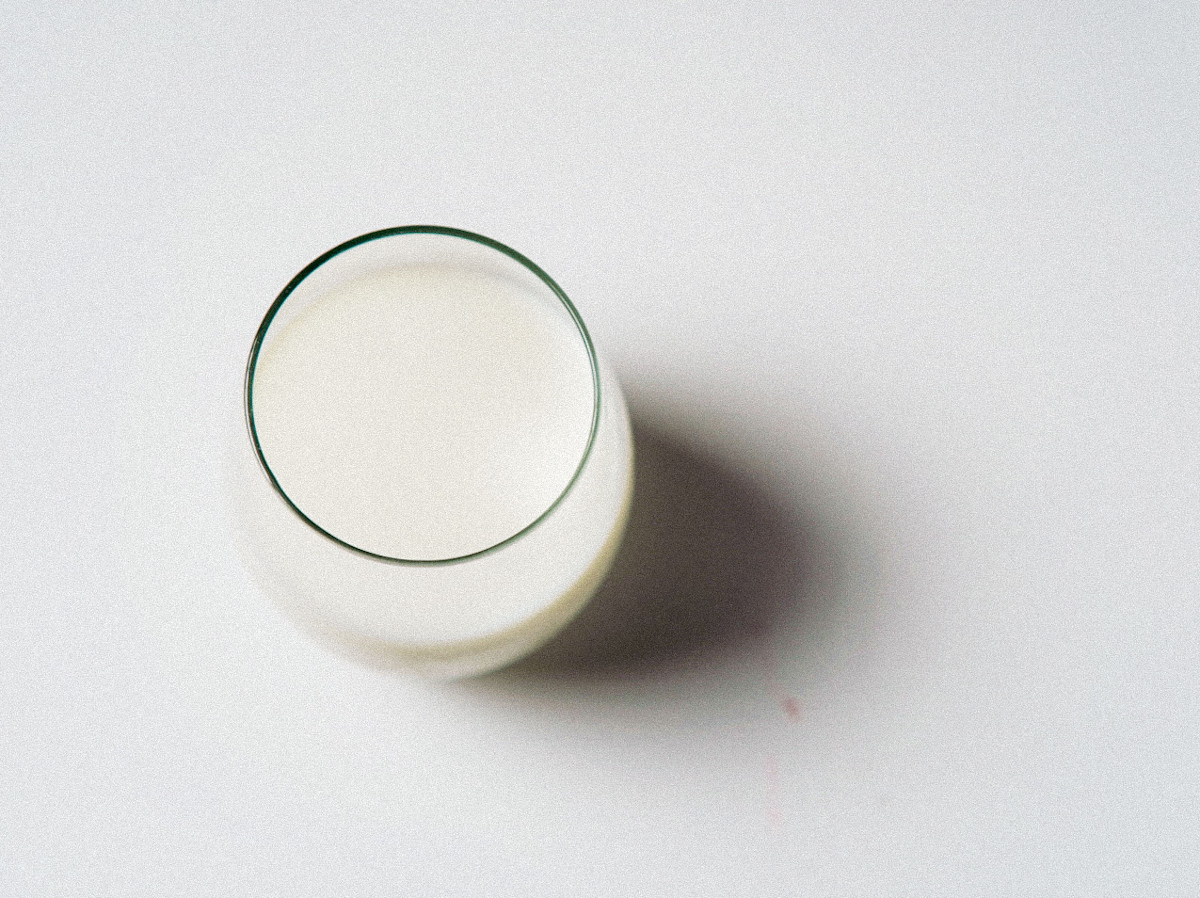 Minimalist image of a glass of milk on a white background, shot from above.