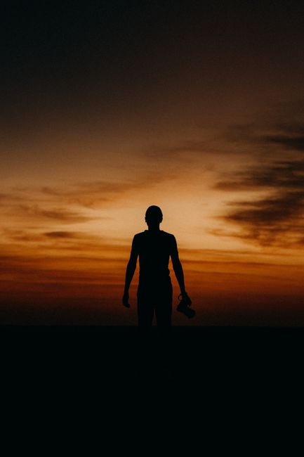 A person stands silhouetted against a dramatic, colorful sunset sky, creating a striking visual.