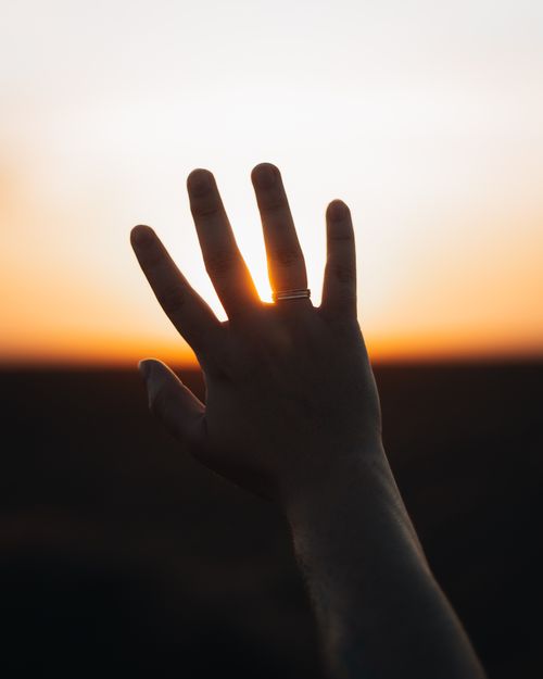 Free A hand with a ring silhouetted against a vibrant sunset sky. Stock Photo