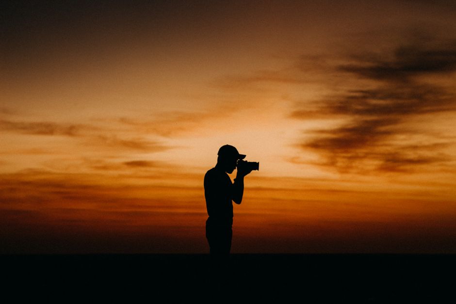 Photographer silhouetted against a vibrant orange twilight sky, capturing the perfect moment.