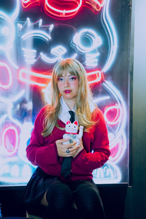 Free A young woman with blonde hair holds a cat figurine against vibrant neon lights. Stock Photo