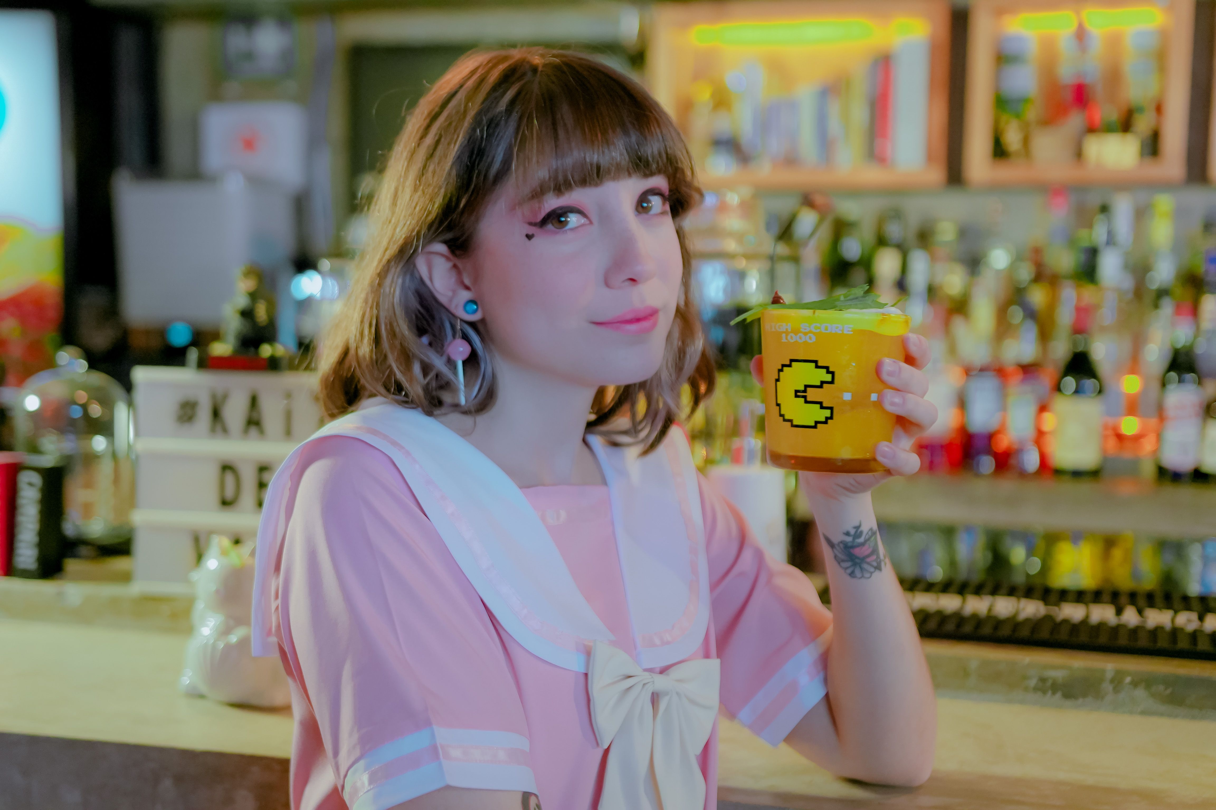 A young woman in a pink dress holds a fun orange drink at a trendy bar.