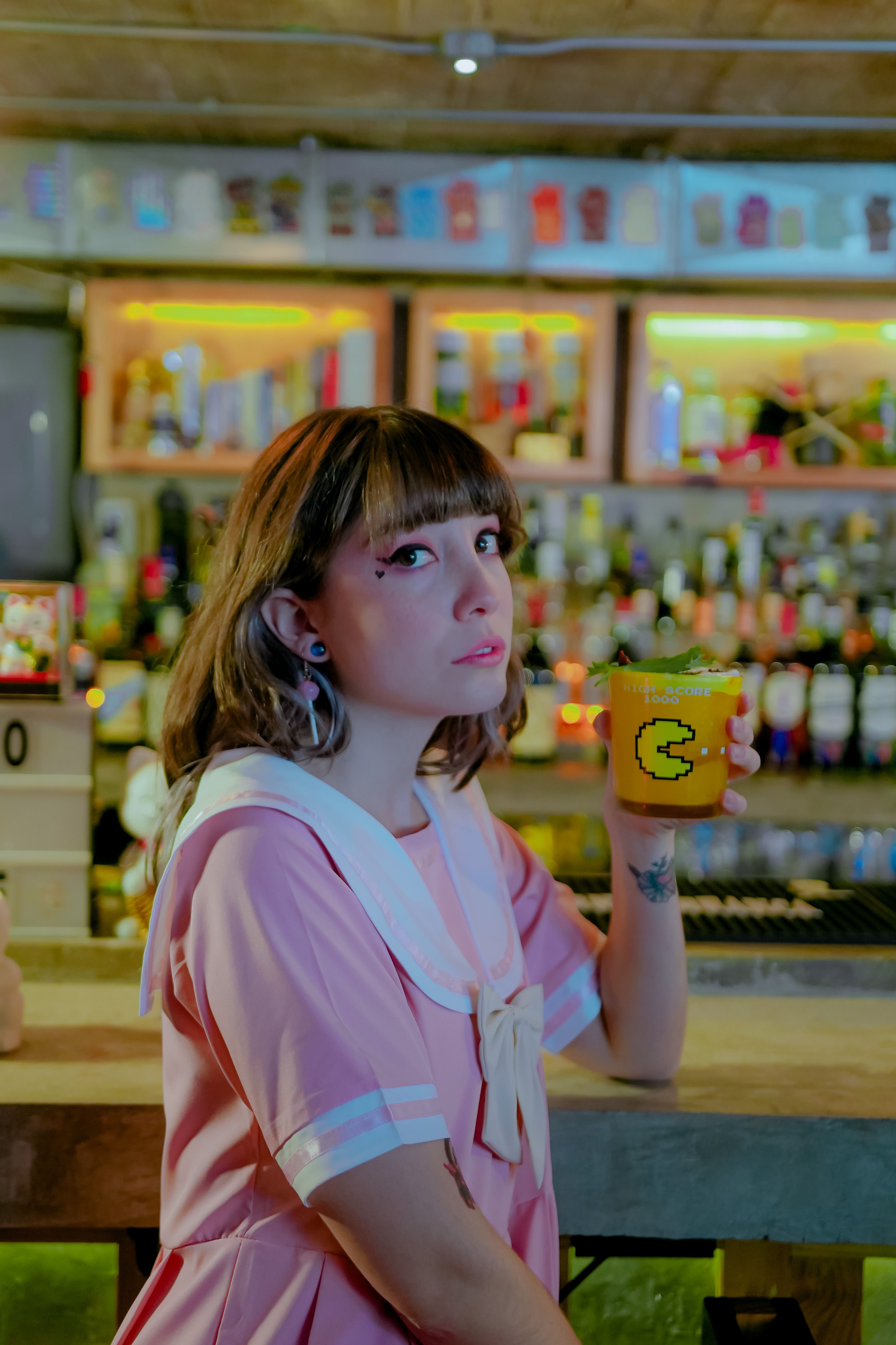 Charming young woman in a retro pink dress enjoying a drink at a stylish Ciudad de México bar.