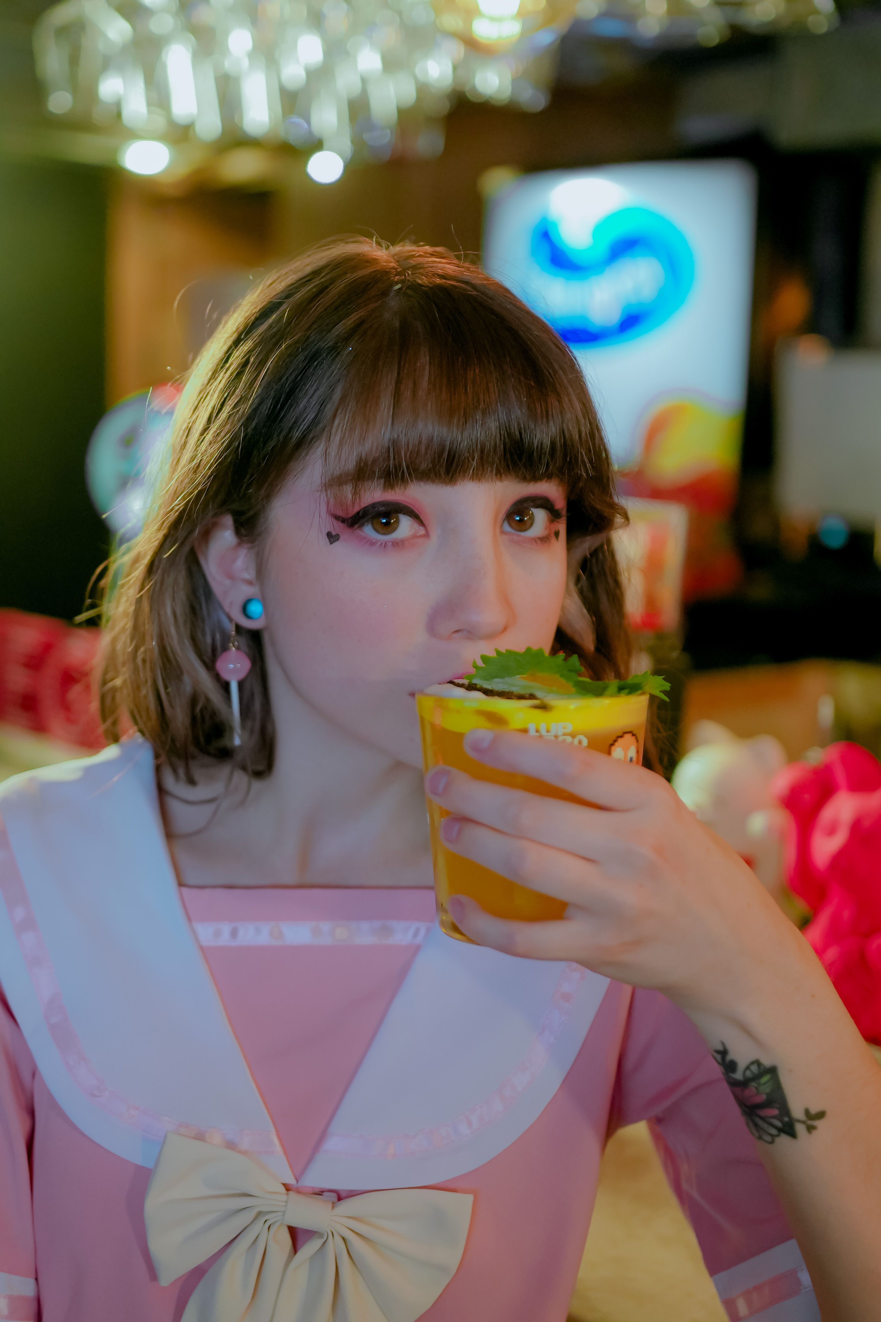 Portrait of a young woman in a pink dress enjoying a vibrant drink indoors.