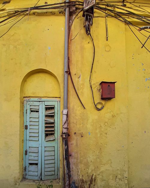 Free A vibrant yellow wall in Kolkata with rustic window shutters and exposed wiring capturing urban decay. Stock Photo