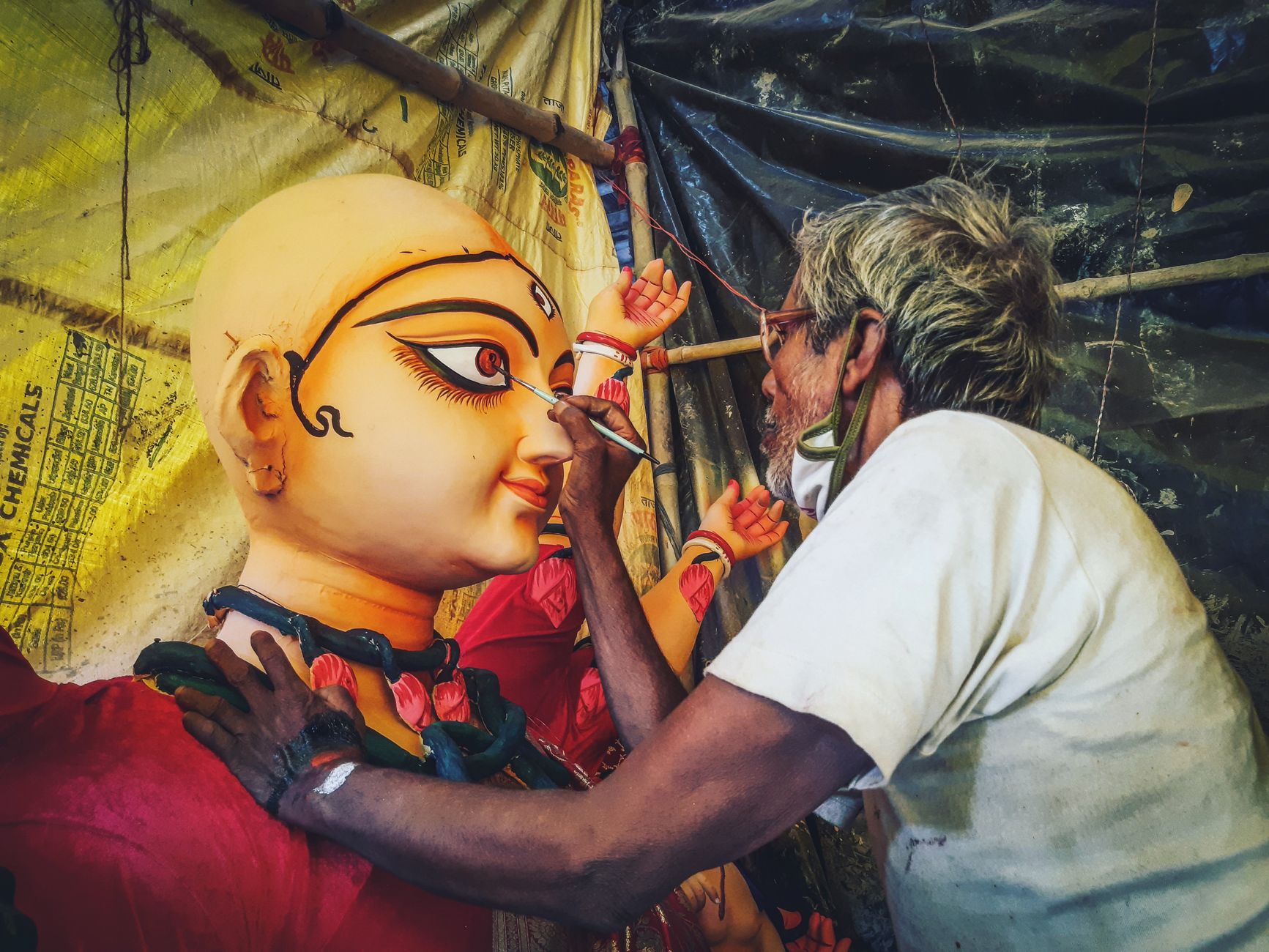 Skilled artisan meticulously painting a Hindu goddess sculpture at a Kolkata workshop.