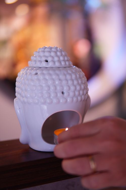 Free Hand lighting a tealight candle in a white Buddha head holder, creating a serene ambiance. Stock Photo