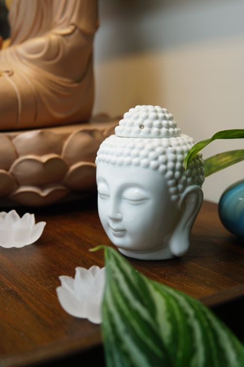 Free A serene white Buddha head statue on a wooden table with green leaves and lotus decoration. Stock Photo