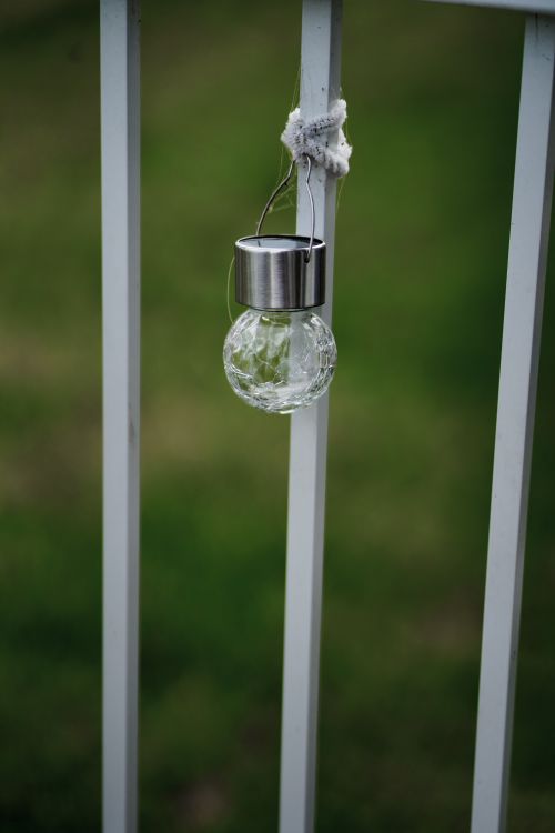 Free Close-up of a decorative glass light bulb hanging on a metal railing outdoors. Stock Photo