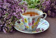 一个带有花卉图案的美丽陶瓷茶杯，里面装满了花草茶，周围环绕着熏衣草花