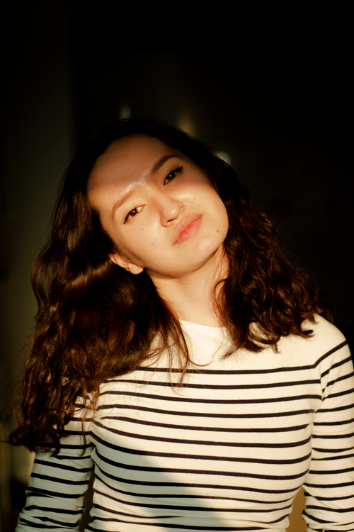 Free A thoughtful woman in a striped shirt is bathed in warm, golden hour light. Stock Photo